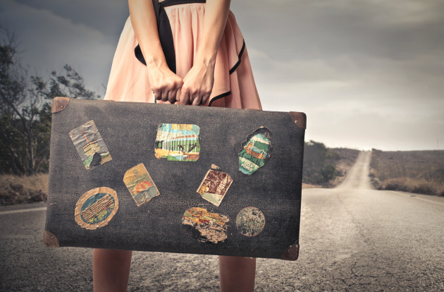 young woman with a vintage suitcase in the middle of a deserted road
